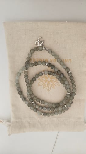 Le client montre son bracelet mala en labradorite gris, posé sur son pochon de rangement.