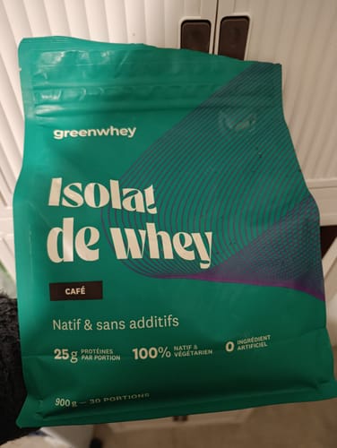 Un client tient le sachet vert d'Isolat de Whey Native saveur café devant un placard blanc.