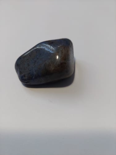 Photo d'un client d'une pierre Dumortiérite foncée et polie, avec des reflets bleus et bruns sur un fond blanc.