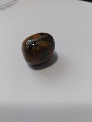 Photo d'un client montrant une pierre de Rhyolite polie et roulée avec des motifs bruns et noirs sur une surface unie.