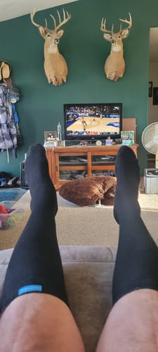 Reviewer relaxing on a couch wearing black Performance Eucalyptus Compression Socks.