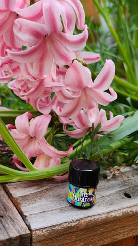 Customer's 'The Huntress' bottle on a wood plank beside blooming pink hyacinths.