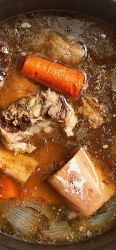 Customer's pot of rich Organic Halal Beef Broth simmering with large beef bones and a carrot.