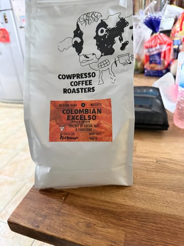 Customer's white pouch of Colombian Excelso coffee beans from Cowpresso Coffee Roasters resting on a wooden surface.