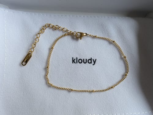 Customer's gold Beaded Chain Anklet laid out on a white fabric pouch.