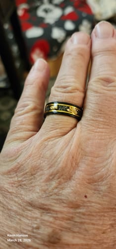 Customer's hand wearing a black ring with gold-colored edges and a patterned inlay.