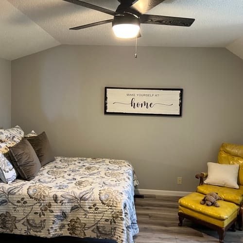 Customer's rustic 'Make Yourself At Home' sign with a black frame hanging in a bedroom above the bed.