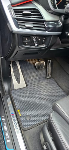 Klient pokazuje ciemny dywanik samochodowy, który jest idealnie dopasowany do pedałów po stronie kierowcy w BMW.