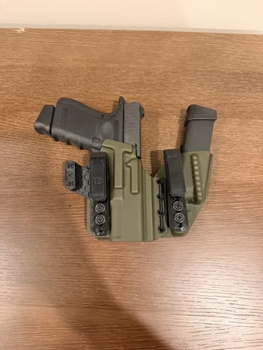 Customer's olive green AXIS ELITE holster holding a pistol and spare magazine, resting on a wooden surface.