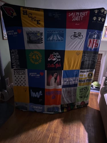 Customer holding up a large, colorful Project Repat T-Shirt Quilt made from a patchwork of many family t-shirts.