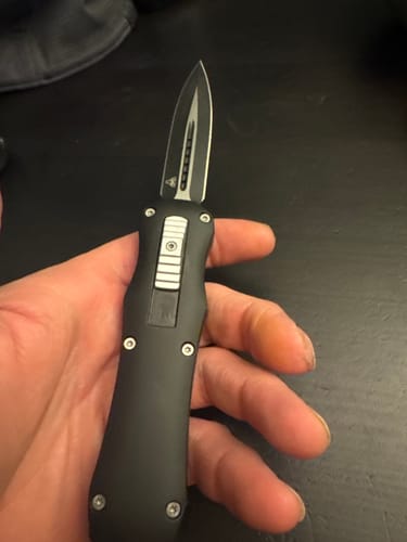 Reviewer holding the Black Reaper OTF Knife in their hand, showing the extended two-tone blade.