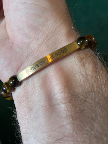 Close-up of a customer's wrist wearing the FOCUS ON THE GOOD bracelet with brown beads and an engraved bar.