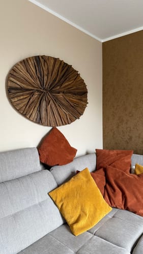 Ein Kunde zeigt die runde LUNAR Wandlampe aus Holz, die an einer beigen Wand über einem Sofa hängt.