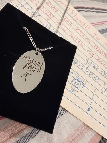 Rezensent zeigt die personalisierte Halskette mit der eingravierten Zeichnung neben dem Originalkunstwerk.