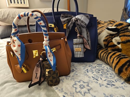 Customer's bronze and navy Warkin Bags sitting side-by-side on a bed, accessorized with scarves and charms.