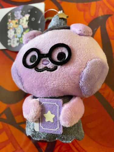 Customer's purple Saniyo plush from the ATEEZ pop-up store, wearing glasses and a sparkly hat and holding a book.