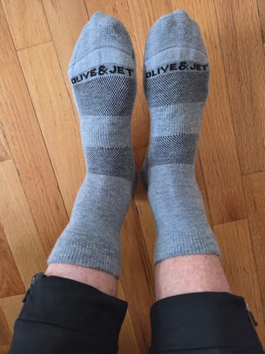 Reviewer wearing the gray striped Quarter Socks, showing the 'Olive & Jet' brand name on top of the feet.