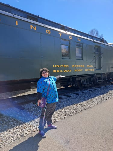 Reviewer standing outside in front of a train, wearing the blue Disney's Tron "Flynn’s Arcade" short sleeve shirt.