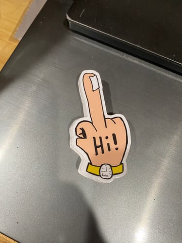 Customer's custom sample sticker of a cartoon hand with a bandaged finger and 'Hi!' on its palm, on a metallic surface.