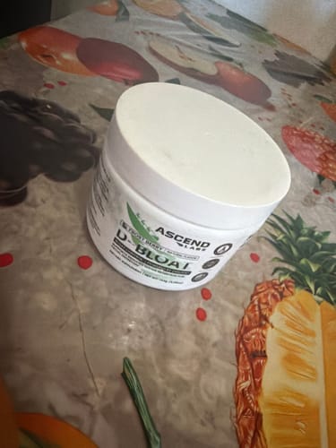 A customer's white tub of D-BLOAT powder resting on a table with a colorful fruit-patterned tablecloth.