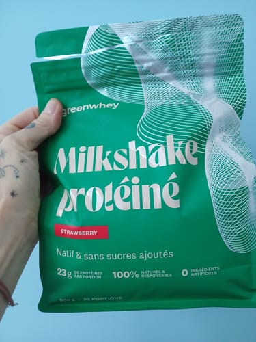 Un client tient dans sa main le sachet vert de Milkshake protéiné à la fraise.