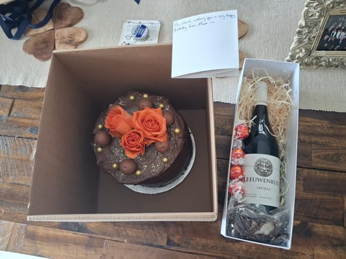Customer's Shiraz and Chocolate gift box displayed on a wooden table next to a large chocolate cake with orange roses.