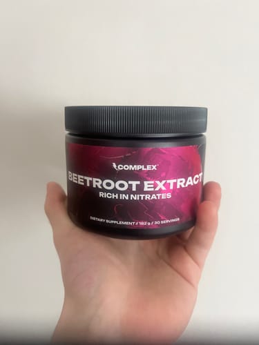 A reviewer's hand holding a black tub of Complex Beetroot Extract supplement against a plain background.