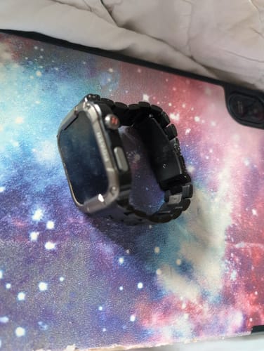 A customer's black steel loop band attached to their smartwatch, resting on a colorful galaxy-print surface.