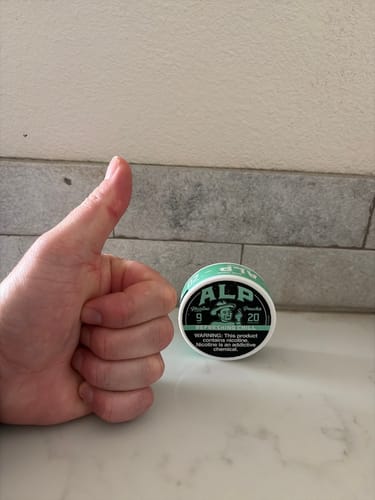 Reviewer gives a thumbs-up next to a tin of Refreshing Chill Nicotine Pouches on a counter.
