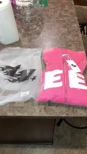 Customer's pink SEEK ZIPUP hoodie, folded on a table next to its original packaging.