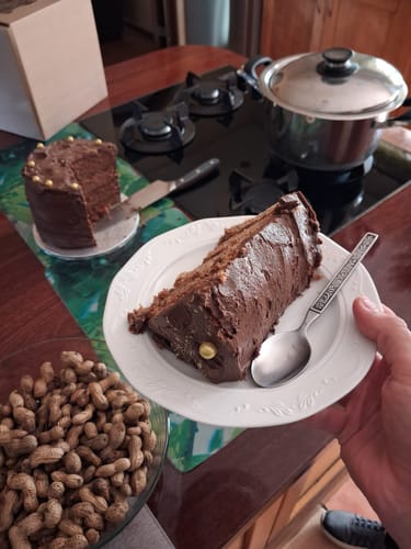 Customer holding a plate with a slice of the rich Decadent Rose Chocolate Cake, with the rest of the cake in the background.