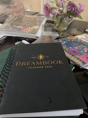 Customer's black 2026 Dreambook + Planner with gold text on the cover, sitting on a cluttered desk.