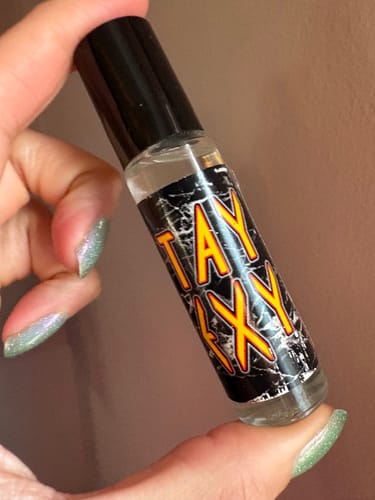 A customer holds the Stay Sexy rollerball perfume bottle, showing its black and yellow label.