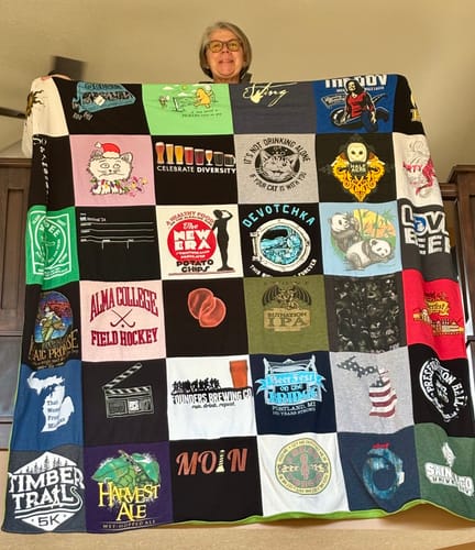 Reviewer holding up their large Project Repat T-Shirt Quilt made from many different colorful t-shirts.