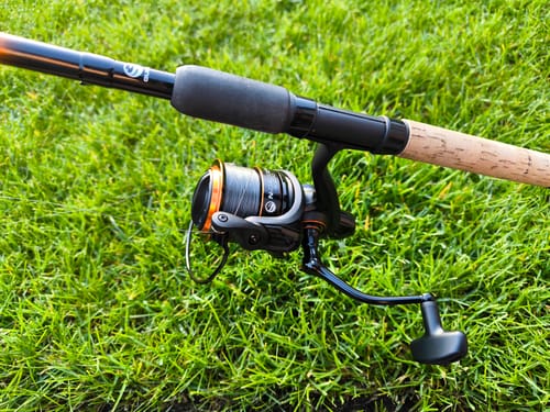 Recensent toont de zwarte N-Gauge Pro Reel gemonteerd op een hengel in het gras.