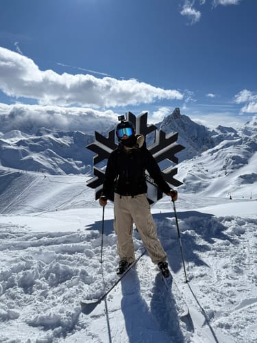 Reviewer wearing the baggy coffee-colored snow pants while standing on skis on a snowy mountain.