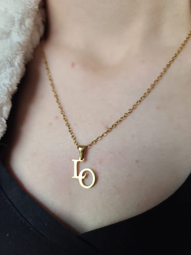 Eine Kundin trägt die goldene, personalisierte Initialen-Kette mit den Buchstaben 'L' und 'O' an ihrem Hals.