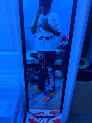 Reviewer taking a mirror selfie while wearing the white EYES TEE in a room with blue lighting.