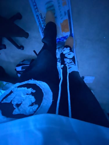 A customer's downward view of their black VISIONZ SWEATS, showing the white graphic detail on the thigh and side stripes.