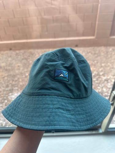 Customer holding up their teal Big Wicking Bucket Hat, showing the front patch.