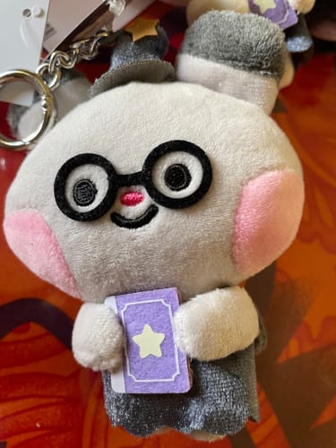 Customer's close-up of the adorable Ddeongyo plush keychain, a white character with glasses and a hat, holding a tiny purple book.