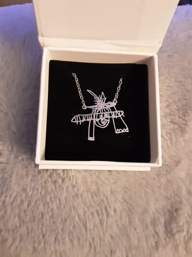 Ein Kunde zeigt die personalisierte Halskette, die nach einer Kinderzeichnung angefertigt wurde, in einer weißen Schmuckschatulle.