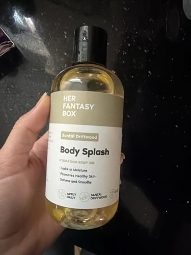 Customer holding the clear bottle of Santal Driftwood Body Splash, showing the golden-colored oil inside.