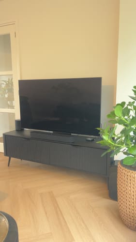 Recensent toont het zwarte TV-Meubel Lima in een woonkamer met een tv erop.
