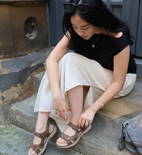 Reviewer sitting on steps, adjusting the strap of their brown Journey sandals for a comfortable fit.