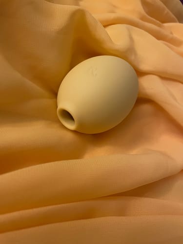 Reviewer's soft, yellow Lem Clitoral Massager resting on a peach-colored fabric.