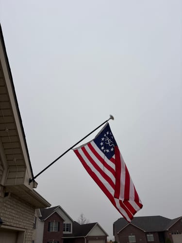 Reviewer's America 250™ Betsy Ross Flag displayed on a pole attached to the side of a house.