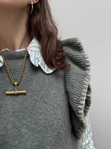 Reviewer showing the gold XL T-Bar Necklace styled over a grey knit vest and a collared shirt.