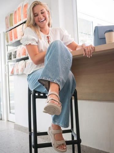 Reviewer laughing while sitting on a stool, wearing their light-colored Journey sandals.