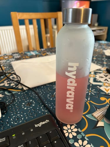 Customer's frosted Hydrava bottle filled with a pink electrolyte drink on a desk.